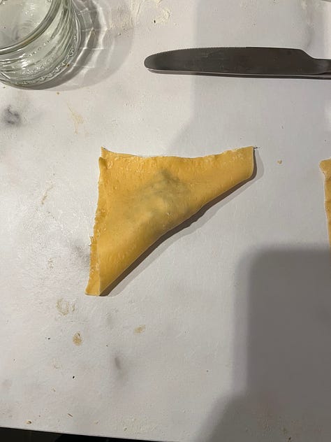 Steps for making tortellini from fresh using a pasta machine illustrated. The pasta is rolled before cut into squares, with a small amount of filling added and then folded into a triangle before the bottom two corners are tied around