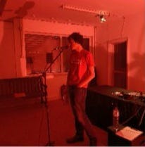 Three images of Stu reading in a room lit by red lights. Location: The Auxiliary Project, Middlesborough. July 2023