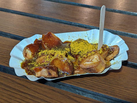 Three images, each of a currywurst in a paper tray. Each one is a cut-up bratwurst covered in ketchup and curry powder.