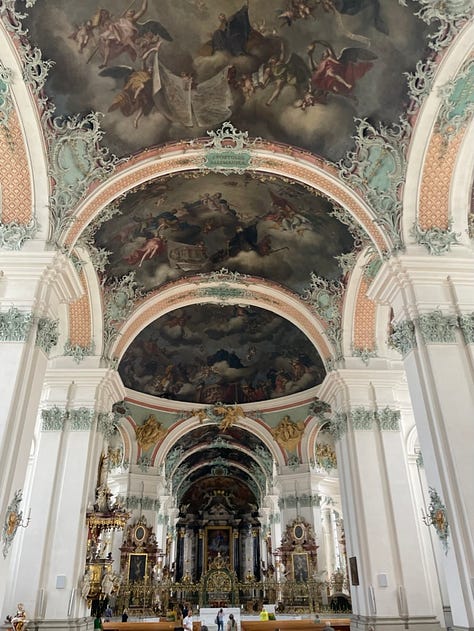 On the left, five people standing in front of a Ferris wheel in Geneva, Switzerland. Two have their hands raised. In the middle, the ceiling of the St. Gallen cathedral, featuring three huge vaults and a dark fresco. The moulding is pink and green. On the right, a goat or antelope rubbing its large horns against a tree in a rocky enclosure.