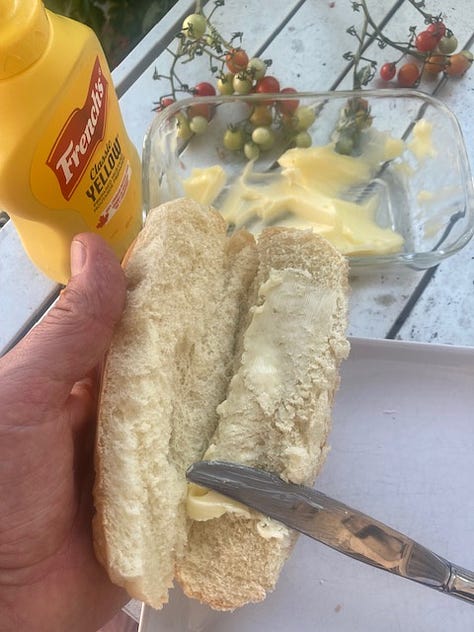 Grilled hotdogs being prepared on an outdoor grill with a number of ingredients and the buns.