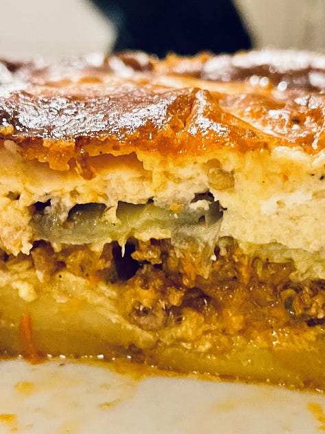 Close-up of a serving of Moussaka, showcasing its creamy béchamel topping and flavorful layers of eggplant, meat, and spices.