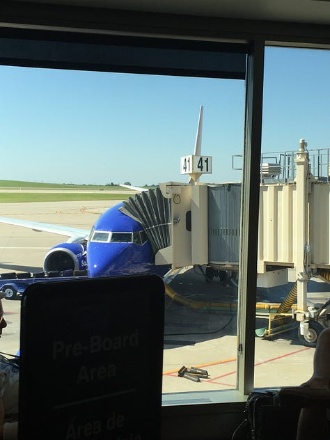 A window framed by a shadowy room, a blue and gold speckled floor, a Southwest airplane at the gate 