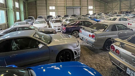 A collection of photos showing dozens of white, blue and green Nissan R34 Skyline GT-R sports cars crammed into a dimly-lit warehouse with gray walls and green support beams with a gravel floor.