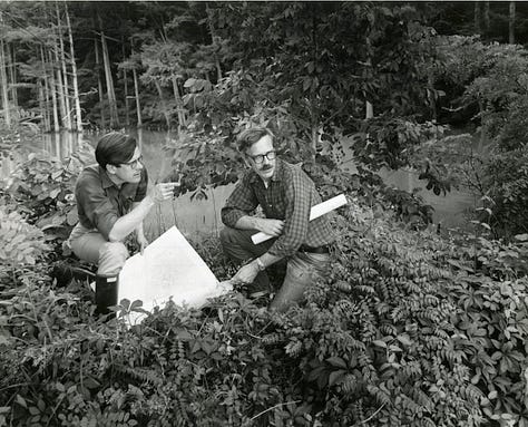 Harold Gill working on plat maps in his office in the Travis House in Colonial Williamsburg's Research Department, part of the York County Project and with Cary Carson following those maps in the now wooded area near Williamsburg. Finally, with the cast of research specialists that stand behind every interpreter in Colonial Williamsburg in the 1970s.