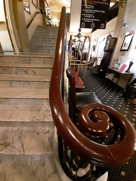 A collage of photos showing the Historic Hotel Bethlehem, including two photos of the 9-story brick exterior, and interior pictures of the elevators, white marble staircase with polished handrail, open doors to the ballroom with a glistening chandelier, and two photos of the lobby, with luxurious black leather furniture in front of a huge arched window with a Christmas wreath in the middle. Also a look inside a room of a bed with a robe lying on the end.