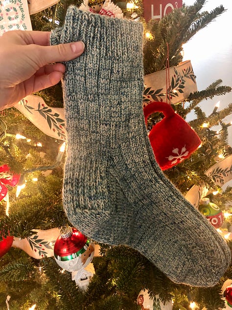 Three marled socks held up in front of a lit Christmas tree.