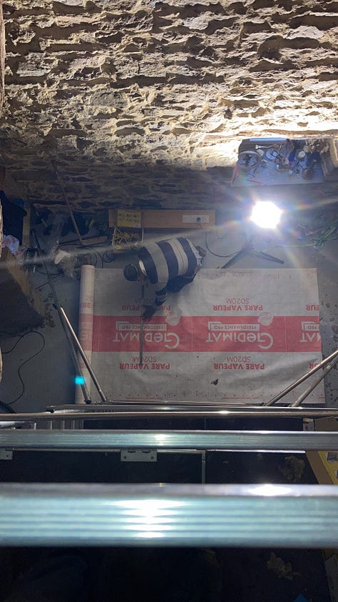 Steve in a breathing mask, glasses, and a black bandana over his hair looks out at us from the top of the scaffold in this selfie. His head is at the apex of the partly insulated roof. 