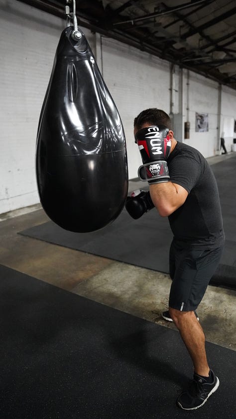 Brian hitting a punching bag at the back of a gym.