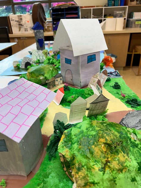 Square cardboard maps are decorated with paint, carved styrofoam, cardboard towers and paper cutouts to depict fantasy environments.