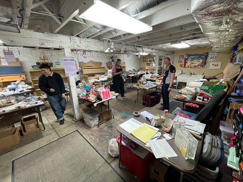 Swappers in a basement space that has filled up with tables and craft materials, clear jars with votes on having the swap again, and a Meadowlark Guide Co coffee mug from a friend who helped arrange materials.