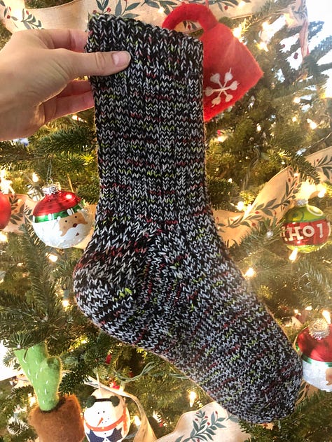Three marled socks held up in front of a lit Christmas tree.
