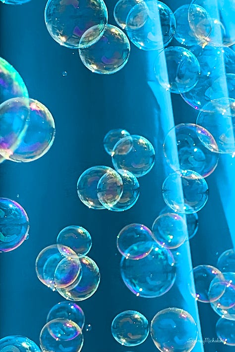 A series of three images features colorful bubbles drifting past a turquoise beach umbrella.