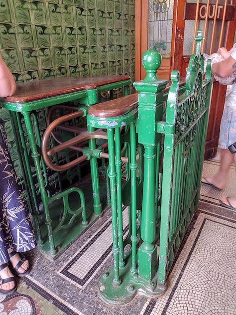 Metal turnstyle, pair of heavy wooden soors with stained glass windows, staircase with walls in tile