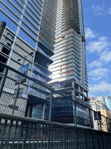 An unfinished building with graffiti running up its seen from a distance and up close balconies against a blue sky