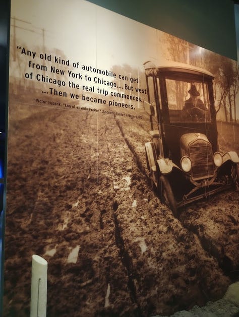 Photo of car driving through extremely deep mud, Model T car from 1920s,Info panel, Model T with mural of motor court behind, mural and tableau of motor court cabins