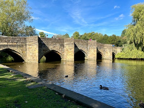 3 photos. 1 The 17th century stone bridge crossing the Rover Wye. Picture 2 the river flowing over a small weir. Picture 3 Trout swimming in the River Wye close to the river bank with ducks swimming above. Images: Roland's Travels