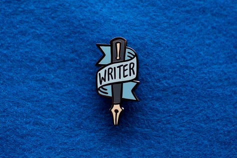 Three enamel pins with the words "WRITER," "PAINTER," and "ARTIST" emblazoned on the front.