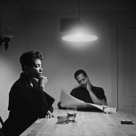 1-9) All images are black and white, and involve a table, as well as a few chairs, and an overhead light. 1) A black woman is seen playing cards by herself. 2) A black woman is seen holding her head in her hands, while reading a book. There is a child sitting to her right, writing. 3) A black person is standing at the end of the table, looking into the camera. 4) A black woman is looking at herself in a tabletop mirror, while a child is playing to the right of her at the table. 5) Three people are sitting at the table, and appear to be playing a game or laughing. 6) A black woman is seen looking at herself in a tabletop mirror. 7) A black woman is sitting on the left side of the table, with her hand under her chin. There is a black man at the end of the table, reading the newspaper, with his hand resting on his neck. 8) Two black people are seen kissing/embracing. One is sitting at the end of the table, and the other person is behind them. 9) A black woman is seen with her head laying back on the table, with her hands in her hair.