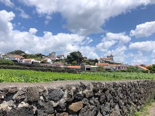 Photos of black rocks in a frothy ocean, a stone wall in front of fields and a village, a town plazaa with colorful buildings and orange tile roofs.
