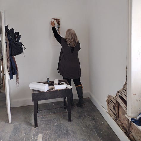 Images of artworks in a dilapidated room, plaster and lath crumbling away from the walls, and artist hanging her work on the wall, a pink flower artfully placed on a mirror and photographed to show reflections of other artworks in the mirrored glass