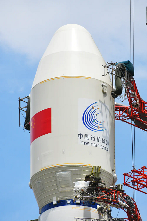 One of the Long March 3B/E's boosters being lifted during preperations, the rockets second-stage following equipment installation, and the vehicles fairing with the asteroid program's logo.