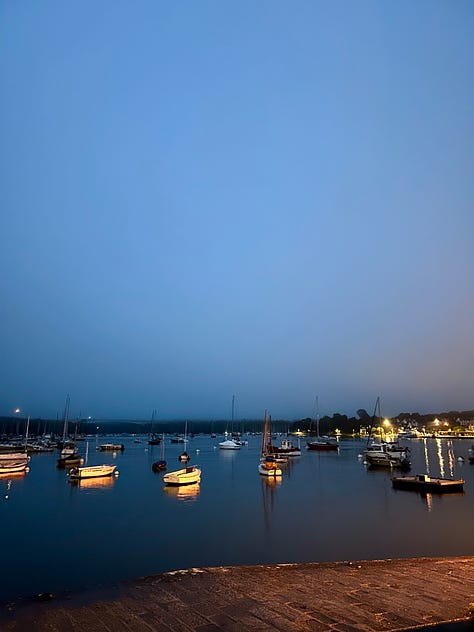 an evening harbor filled with boats; restaurant sign offering oysters and wine, a seafood platter; a breakfast picnic basket