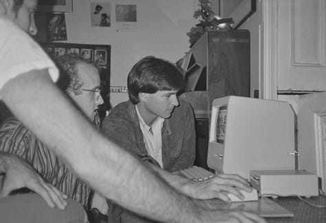 Steve Jobs le enseña a utilizar uno de los primeros Macintosh a Sean Lennon, mientras Keith Haring y Andy Warhol observan.