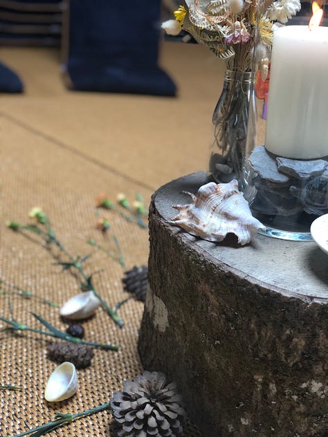 1. Circle centrepiece with a log, flowers, shells and a candle. 2. A small altar with a large shell, a candle in a tin, pinecone, feather, selenite crystal, moss stick and a stone. 3. A hand with a lotus tatoo at the wrist holding a small white bowl with dried rose petals, small shell, ceramic butterfly and pinecone.