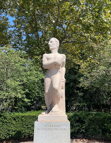 large limestone sculptures in an outdoor sculpture garden against a blue sky depicting a laborer, a scientist, and a poet