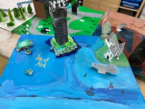 Square cardboard maps are decorated with paint, carved styrofoam, cardboard towers and paper cutouts to depict fantasy environments.