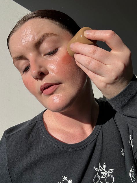 Morgan applies a cream peach blush to her cheeks and uses fingers to blend them out