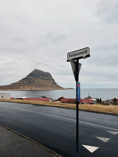 Three images from our time in Grundarfjörður.  1st is our kitchen for the night with light wood cabinets, a small sink, two burners on the countertop and a tiny black refrigerator. 2nd and 3rd views from our walk around town, the mountain as seen from a street looking across the water and small white church with a red roof and tall steeple also painted red.