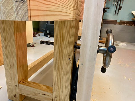 My workbench upside down on a table, the vice installed and a hand plane making shavings to flatten the bench top.