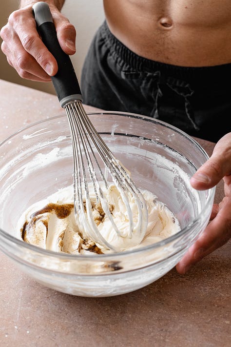 Making vegan cream cheese frosting in a glass bowl with a whisk on a red counter