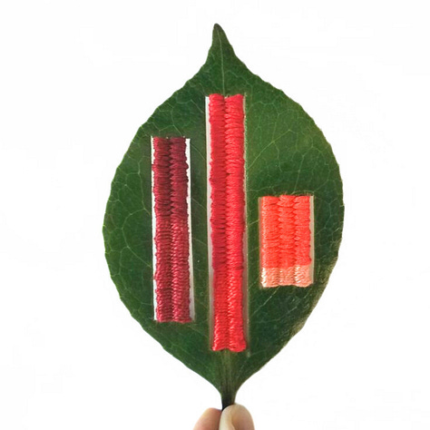 three leaves with thread woven or stitched on.