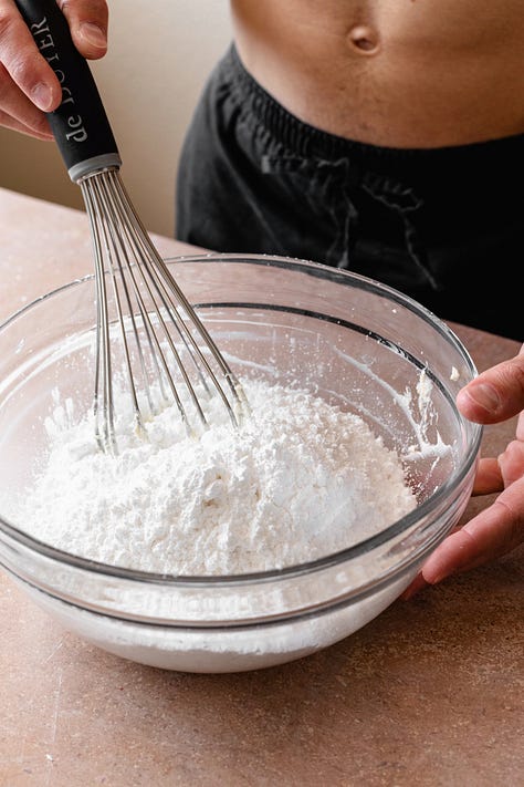 Making vegan cream cheese frosting in a glass bowl with a whisk on a red counter
