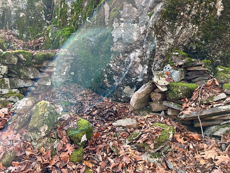 A stone construction in the woods against a cliffside.