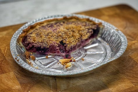 Three photos from left to right. First, the remains of the peach-blueberry pie in its pie tin. We can see the brown crumble top and the dark purple filling. Next, a hand holding a butter tart that has a bit taken out of it. we can see creamy golden filling and the dark pecans on top, as well as the slightly flaky pastry. Finally a baby pickle on a fork with a bite taken out of it. It... looks like a pickle with a bite taken out of it. Nothing special (just l like the flavour).