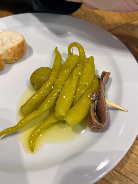 anchovies and blue cheese on a bed of fried onion, a bar meat station with hanging jamon and wrapped cheese, pickled peppers, olives and anchovies on a toothpick