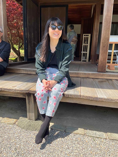Left: Jenny in a blue sweater and dark jeans on a bike with some tulips. Center: Jenny in an all-black getup with sunglasses, a mask, and tote bag. Right: Jenny sitting outside in some cherry blossom pants and blue-gray sweater.