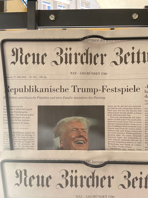 A marquee surrounded by tree branches in Germany; Ellie and Clay horse around in Germany; a castle on a hill in Austria; a German language newspaper with a smiling, injured Trump on the front page; a storefront featuring pillows embroidered with fancily dressed cats; Cole and Clay retrieve a soccer ball from a construction ditch