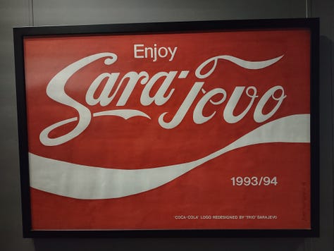 The top left image shows a black poster with barbed wire rings in the form of the olympic rings. It says "welcome to the olympic games. Welcome to Sarajevo". The top middle image shows a sign that says "enjoy Sarajevo. 1993/94" in the shape of the coca-cola logo. In the bottom it says "coca-cola logo redesigned by trio sarajevo". The top right image shows a picture of a Campbell's Soup can that says "Sarajevo';s condensed chicken with rice soup." The cna has bullet holes in it. Underneath it says "Andy Warhol Campbell Soup redeisnged by Trio Sarajevo." The bottom left image shows a poster on a blue background with the united nations logo. It says "1993. Disunited nations of Bosnia and Herzegovina." The bottom right image is of a woman on a black background with stars in her hair. She is sleeping. It says "wake up, Europe! Sarajevo calls every man woman and child."