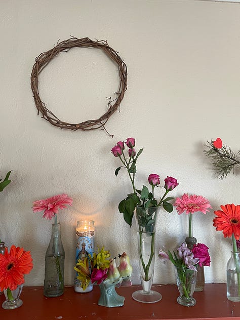 a dried milkweed pod hanging from a vine, a mantle of small stems of flowers in individual bottles and vases, and a person's hand holding a single daffodil