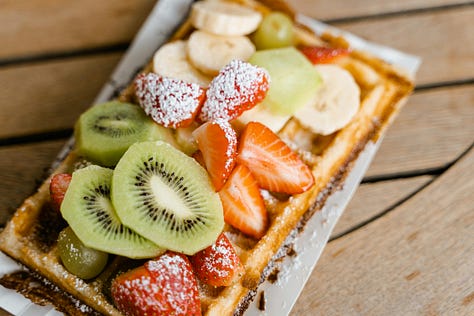 A gallery of photos, a loaf of rustic bread, a table with croissants, two seeded buns, a bowl of chocolate mousse, a scoop of vanilla and chocolate ice cream in a stemmed glass and a crunchy waffle topped with slices of fruit.