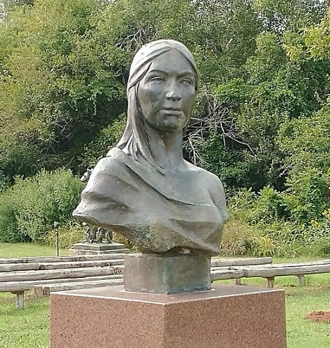 Outdoor sculpture park with metal sculptures of wolves, bears, famous indigenous Americans and a park bench. Flat metal sculptures of bison resemble a small herd across a prairie field.