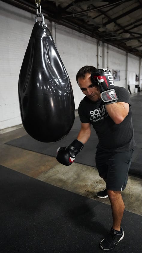 Brian hitting a punching bag at the back of a gym.