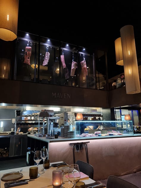 Photo 1: view from our table at Maven showing the sides of beef hanging to dry age and the meat select counter at ground level. Photo 2: photo of Dave in the kitchen talking to 3 Maven chefs. Photo 3: photo of main course including Angus steak, Wagyu steak, frites, and caesar salad.