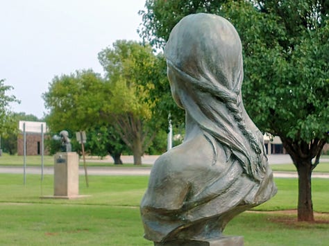 Outdoor sculpture park with metal sculptures of wolves, bears, famous indigenous Americans and a park bench. Flat metal sculptures of bison resemble a small herd across a prairie field.