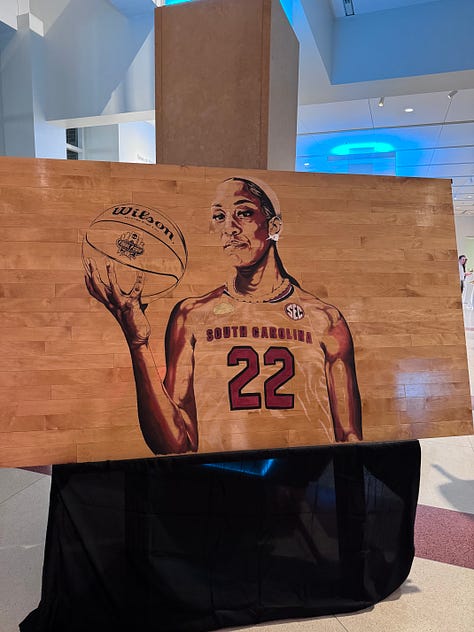 Me and A'ja's statue; custom art of A'ja; Dawn Staley, the artist of the painting shown, and A'ja; poster from the event I attended; A'ja decal on the arena; me and Janel; posing in my A'One shirt; A'ja's retired jersey; Dawn Staley Way